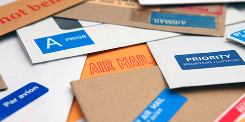 Secure End to End Mailing & Fulfillment Stack of letter envelopes of various colors, with air mail, stamps and postage marks